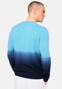 Pull en dégradé de bleu avec une texture côtelée, passant d'un bleu clair à un bleu foncé. Fini avec un ourlet et des poignets côtelés.