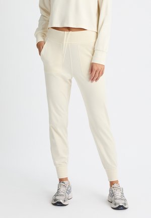 Pantaloni jogger crema con gambe affusolate, vita elastica, cordoncino e tasche laterali. Texture liscia con un finish in tessuto morbido e leggero.