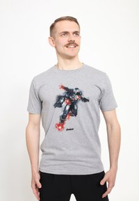 Camiseta de algodón gris con un gráfico colorido de un superhéroe en una pose dinámica con explosiones, logo mostrado en la parte inferior.
