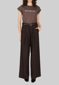 T-shirt marron avec le texte "Pont des Arts", associé à un pantalon noir taille haute et à coupe large, et une ceinture noire. Des talons noirs complètent le look.