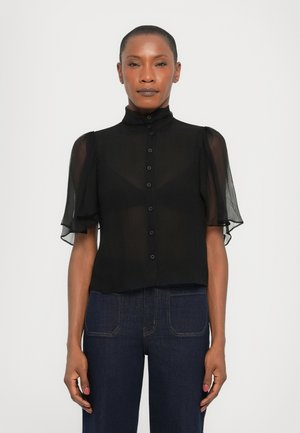 Black sheer blouse with short puff sleeves, button-up front, high collar, and a slightly cropped design. Worn with dark denim pants.