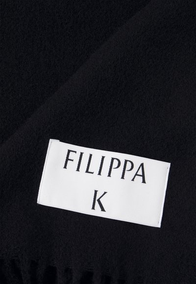 Fekete bolyhos anyag, amelynek puha szálakból álló textúrája van. Egy fehér címke olvasható "FILIPPA K" felirattal, amely az anyag széléhez közel van belevarrva.