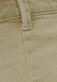 Ljus beige tyg med en fin diagonalt vävd struktur. Har sydda sömmar och en närbild av en midjebandsetikett.