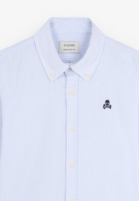 Camisa de botones rayada en azul claro con cuello, que presenta pequeños botones blancos y un logo de calavera y huesos cruzados en negro en el lado izquierdo del pecho.