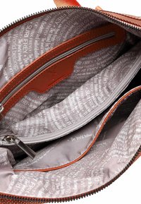 Brunt indre af en taske med en glat tekstur, med en lynlåslomme og svagt, gentaget tekstmønster i lysegrå.