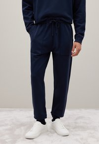 Marineblaue Jogginghosen aus weichem Material, mit einem elastischen Bund und Kordelzug, zwei Seitentaschen und gerippten Bündchen.