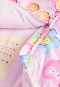 Tissu rose coloré avec de mignons motifs de nuages en bande dessinée. Présente une fermeture zippée et une doublure en polaire douce. Étiquette d'entretien visible.