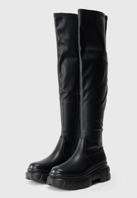 Μαύρες μπότες μέχρι το γόνατο φτιαγμένες από λείο συνθετικό υλικό, με χοντρό, ογκώδες πάτο και φερμουάρ στο πλάι για εύκολη χρήση.