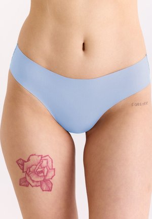 Unterkörper in hellblauer Unterwäsche, zeigt Tätowierungen: eine rosa Rose auf dem linken Oberschenkel und den Schriftzug "FOREVER" an der rechten Hüfte.