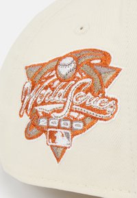 Beige cap featuring embroidered "World Series" logo in orange, grey, and white, with a baseball motif and peak stitching detail.