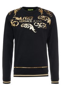 Sweatshirt noir avec des motifs floraux dorés et la marque "VERSACE JEANS". Comprend des bandes dorées métalliques aux poignets et à l'ourlet.