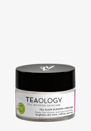 Teaology Tea Glow Blemish Cream in een doorzichtige pot met een zwarte deksel. Het etiket heeft een groen theemotief, tekst en een roze accentstreep.