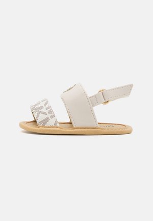 Lysebeige sandal med en struktureret hvid rem og justerbar ankelrem. Har en komfortabel, flad sål og minimalistisk design.