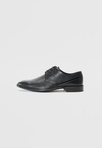 Chaussure noire en cuir avec un bout pointu, présentant un design texturé et des accents de panneaux lisses. Comprend cinq œillets pour les lacets.