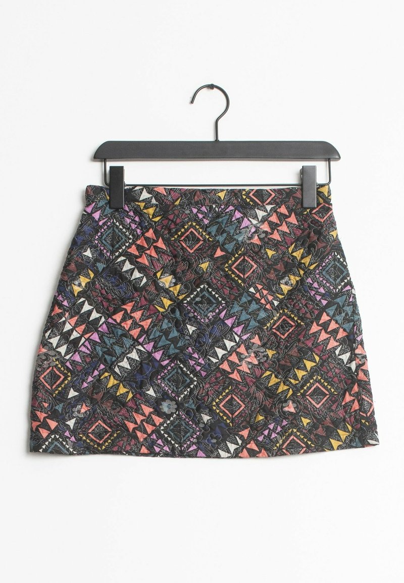Jupe mini multicolore avec des motifs géométriques en violet, rose, noir, bleu et jaune. Fabriquée en tissu texturé, elle est suspendue à un clip noir.