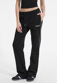 Black sweatpants with elastic waistband and drawstring, featuring side stripes, pockets, and embroidered logo on the front.
