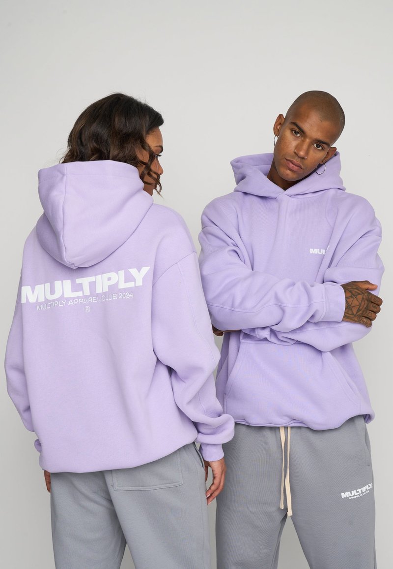 Sudaderas lavanda con una textura suave, con el logo "MULTIPLY" en la parte trasera. Combinadas con pantalones de chándal grises sueltos y un diseño de bolsillo frontal.