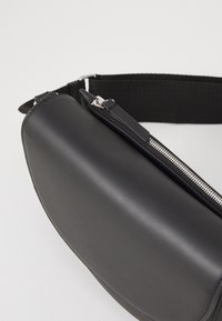 Borsa a tracolla nera in pelle con cerniera argentata e tracolla in tessuto regolabile su sfondo bianco.