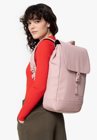 Pink backpack with a fold-over flap, adjustable straps, and minimalistic design. Material appears soft with a smooth texture.