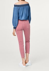 Top in denim con spalle scoperte e scollatura arricciata, abbinato a pantaloni rosa a cropped e sneakers bianche. Tessuto morbido, stile aderente e design casual.