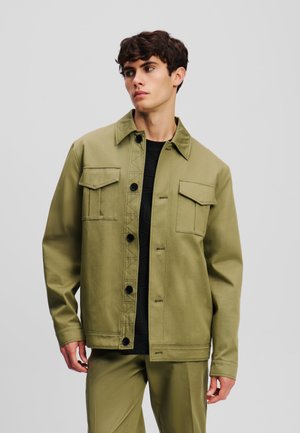 Olive green jacket made of sturdy fabric, featuring a button front, two chest pockets, and a collar. Smooth texture with a relaxed fit.
