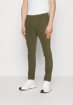 Oliwkowe chinosy w slim fit wykonane z miękkiego materiału, z płaskim przodem, szlufkami na pasek i zwężanymi nogawkami, połączone z białymi trampkami.