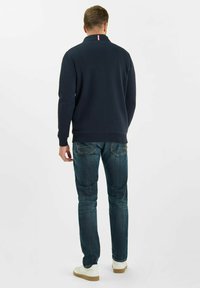 Felpa navy con colletto alto, polsini e orlo a coste. Abbinata a jeans blu scuro e sneakers bianche. Striscia rossa, bianca e blu al colletto.