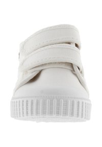 Sneaker bianco in tela con due cinturini in velcro regolabili, suola in gomma testurizzata e design con punta arrotondata. Struttura leggera e semplice.