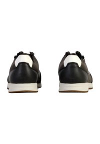 Zapatillas de cuero negras con acentos blancos, puntera redonda, suela de goma plana y lazo decorativo en la parte trasera. La vista trasera destaca el diseño y los materiales.