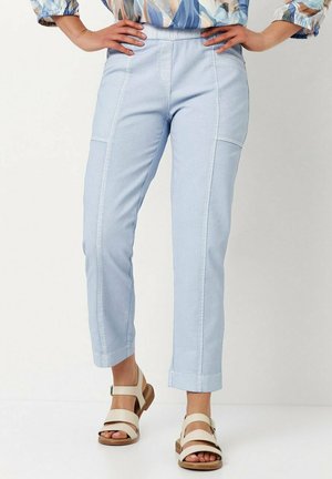 Light blue jeans with a tapered fit, featuring front seams, patch pockets, and a cropped hem. Paired with tan strappy sandals.