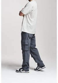 Bílá bavlněná tričko, šedé cargo kalhoty s bočními kapsami a černobílé tenisky. Ležérní design, pohodlný střih a lehká textura.