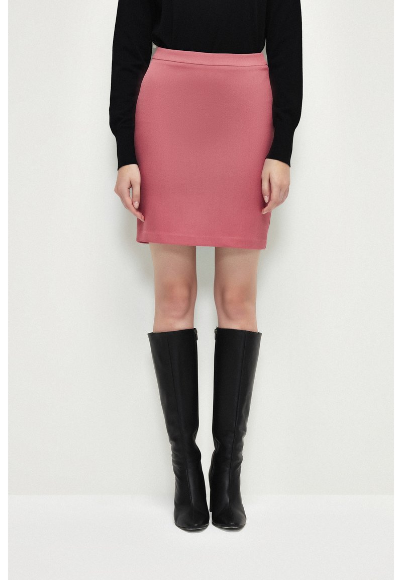 Roze aansluitende rok in een geweven stof, gecombineerd met zwarte leren laarzen tot op de knie. Eenvoudig ontwerp met een gladde tailleband.