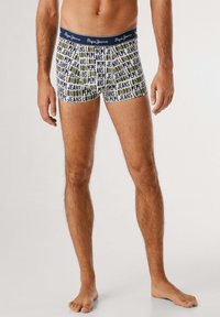 Männliches Model, das weiße Boxershorts mit einem Textmuster "Pepe Jeans London" und einem navyblauen Bund mit dem Logo "Pepe Jeans" trägt.