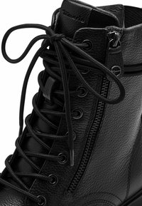 Black leather ankle boot featuring a textured surface, front lacing, and a side zipper closure with metallic accents.