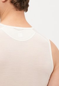 Fehér ujjatlan top strukturált hálós mintával és kerek nyakkal, kontrasztos díszítéssel a nyakrészen és a karöltőkön.