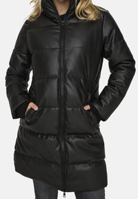 Zwarte pufferjack gemaakt van glad faux leer, met een hoge kraag, ritssluiting, twee voorzakken en geribbelde manchetten.