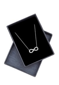 Sølv kædehalssmykke med et infinity-symbol vedhæng udsmykket med klare rhinsten, præsenteret i en gaveæske med sort fløjl.