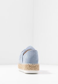 Ljusblå mocka espadrille-sko med vävd jute-mittsåle och vit gummiyttersula, visad från baksidan på vit bakgrund.
