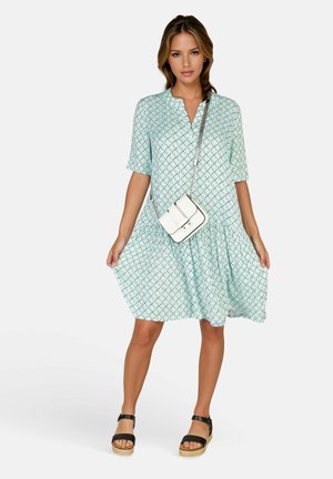 Lichtblauwe jurk met patroon, korte mouwen, V-hals en een geplooide taille, gecombineerd met een witte crossbody tas en zwarte plateausandalen.