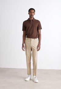 Brun polo skjorte med krage, beige skreddersydde bukser og hvite sneakers. Glatt stoff, tettsittende design, med tydelig fargekontrast.