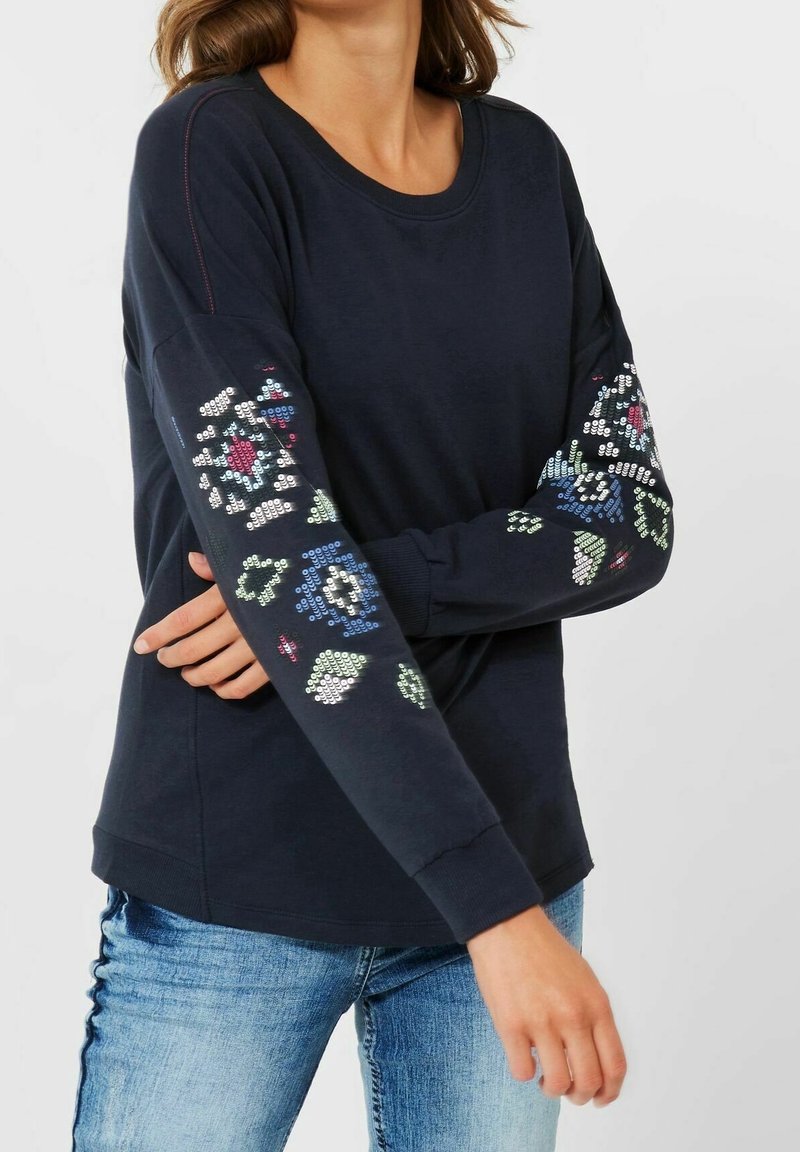 Maglietta a manica lunga blu navy con motivi floreali in paillettes sulle maniche. Tessuto morbido, collo a giro e polsini a costine. Vestibilità casual.