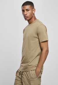 Khaki bomull t-skjorte med rund hals og korte ermer. Stoffet er glatt med en avslappet passform, kombinert med lyse khaki shorts.