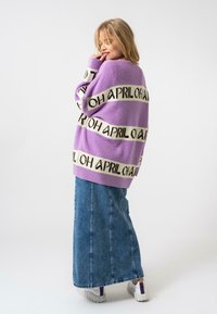 Pull tricot lilas avec le texte noir et blanc "AVRIL" sur de larges rayures. Assorti à une longue jupe en denim et des baskets blanches.
