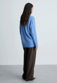 Maglione oversized blu chiaro con orlo a coste, abbinato a pantaloni larghi marroni. Tessuto liscio, maniche lunghe e vestibilità comoda.