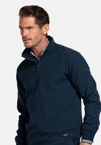 Navy blauwe ritsloze pullover van textuurstof; voorzien van een hoge kraag, chunky ribgebreide manchetten en een logoaccent vlakbij de zoom.
