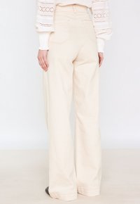 Pantalons larges en crème en coton, avec une taille haute, des poches arrière et des détails de couture en contraste. Texture lisse.