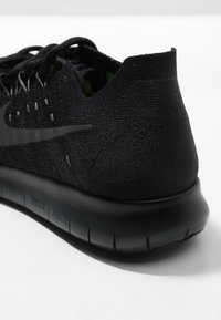 Chaussure de sport noire avec une tige en maille texturée, un col rembourré et une semelle flexible. Caractérisée par un logo Nike noir et un intérieur vert.