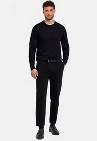 Schwarzer langärmeliger Pullover, eng anliegende schwarze Hose und dunkle Schuhe mit glatter Textur. Einzelmodell, neutraler Hintergrund.