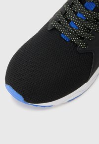 Melna sporta kurpe ar teksturētu sietu augšdaļu, zilām akcentām uz pirksta un mēles, un tumši zaļām šņorēm ar maziem punktiem. Balta zole.