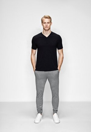 Sort v-hals t-shirt, grå joggers med elastiske manchetter og hvide sneakers. Glat stof med en slim fit, stående foran en neutral baggrund.